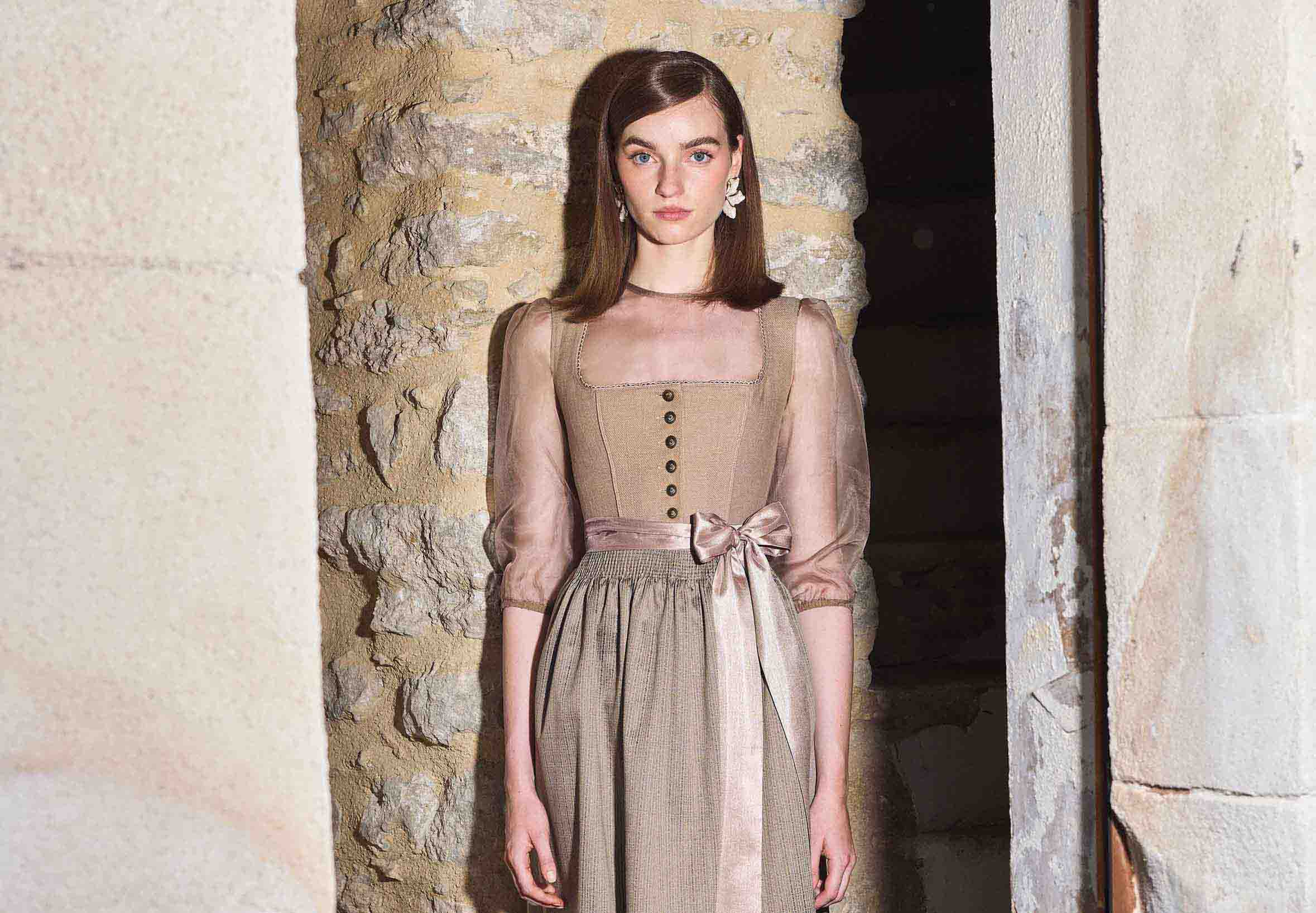 Frau trägt ein beiges Dirndl mit einer hochgeschlossenen Dirndlbluse.